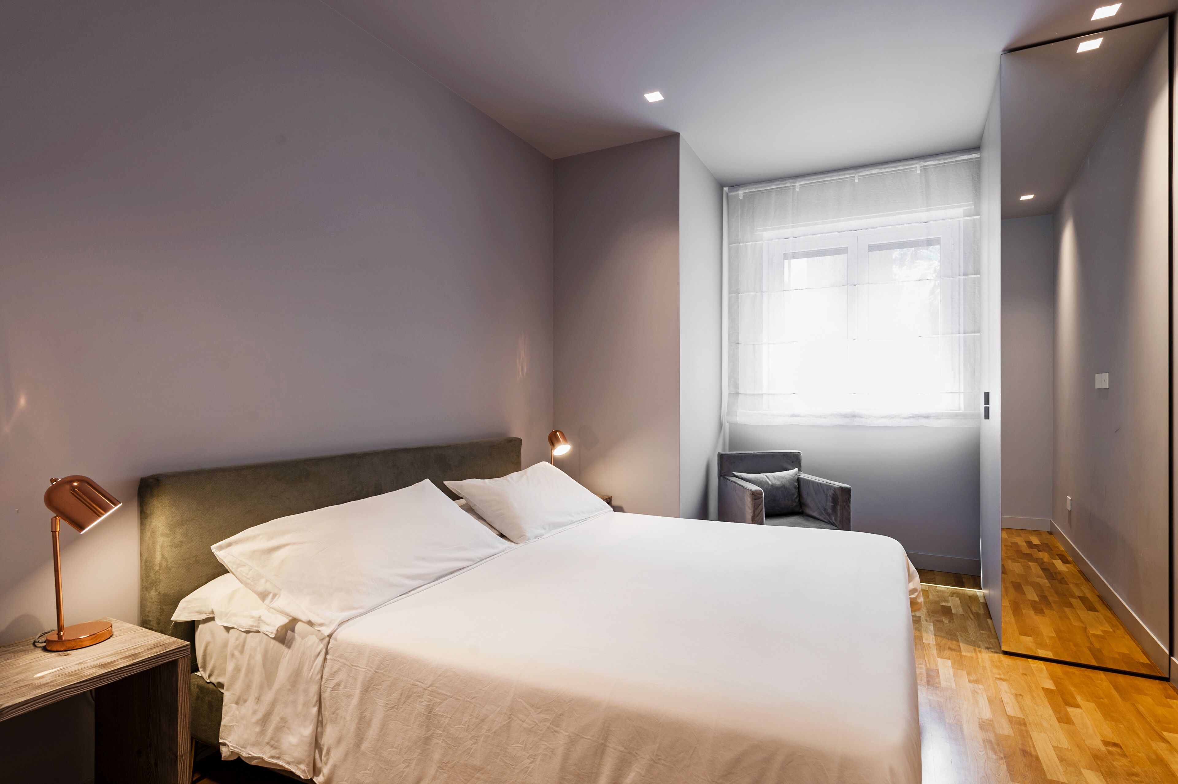 Un dormitorio moderno con una cama grande, lámpara de noche y ventana con cortinas de gasa.