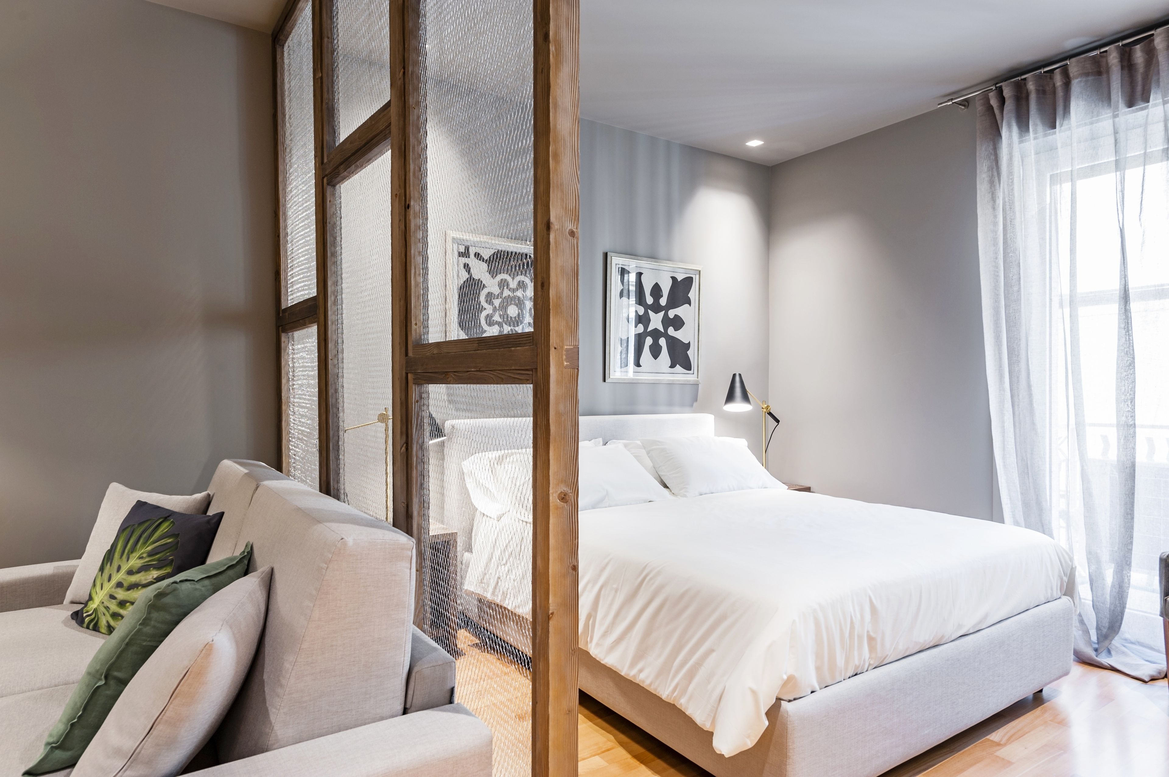 A modern bedroom with a large bed, a sofa, and a window with sheer curtains.