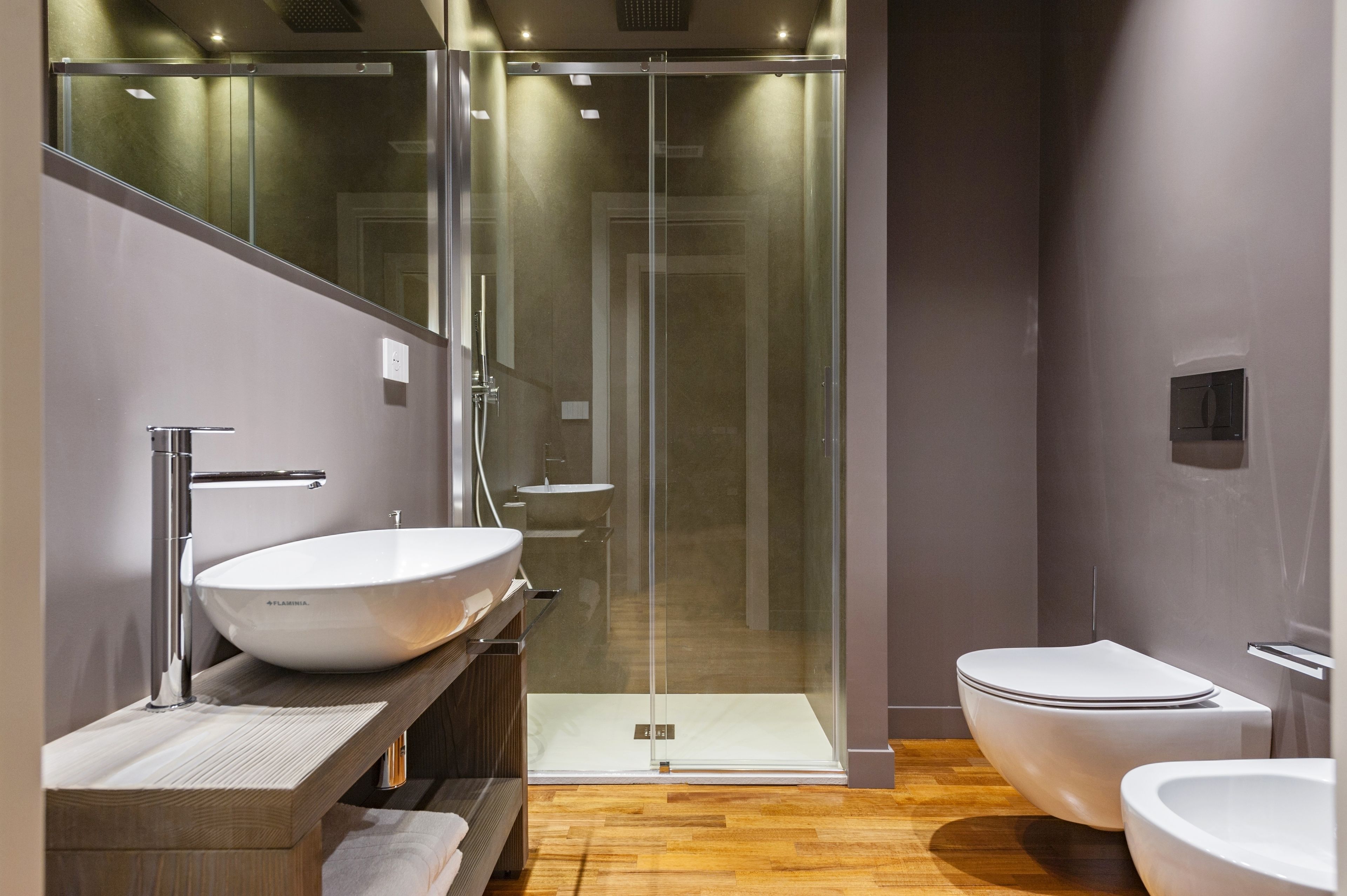 Un baño moderno con ducha de vidrio, un lavamanos blanco grande y un inodoro.