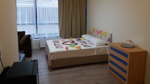 Habitación de hotel con cama, escritorio, cómoda y ventana con cortinas.