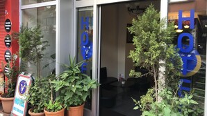 Entrada de hotel con puerta de cristal, plantas en macetas y un letrero.