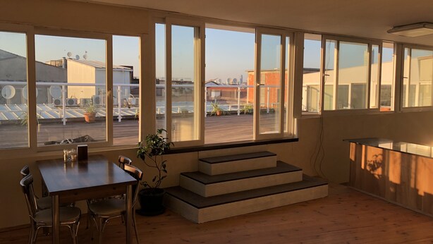 Una habitación moderna con ventanas amplias, una mesa de comedor, sillas, una planta en maceta y una escalera.