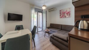Ein modernes Wohnzimmer mit Flachbildfernseher, einer Couch, einem Esstisch mit Stühlen und einem kleinen Beistelltisch.