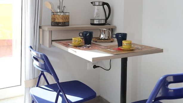 A small kitchenette with a table, chairs, a coffee maker, and a shelf with books and flowers. - VILLA ROSA - Apartment n. 5 "MYRTLE" (2 beds): (Napoli)