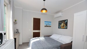 A bedroom with a bed, a bedside table, a lamp, a painting, and an air conditioning unit. - VILLA ROSA - Apartment n. 5 "MYRTLE" (2 beds): (Napoli)