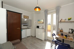 A compact kitchen with a microwave, sink, and cabinets, a dining area with a table and chairs, and a door leading to another room.