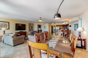 A spacious living area with a dining table, wooden chairs, a sofa, and a TV.