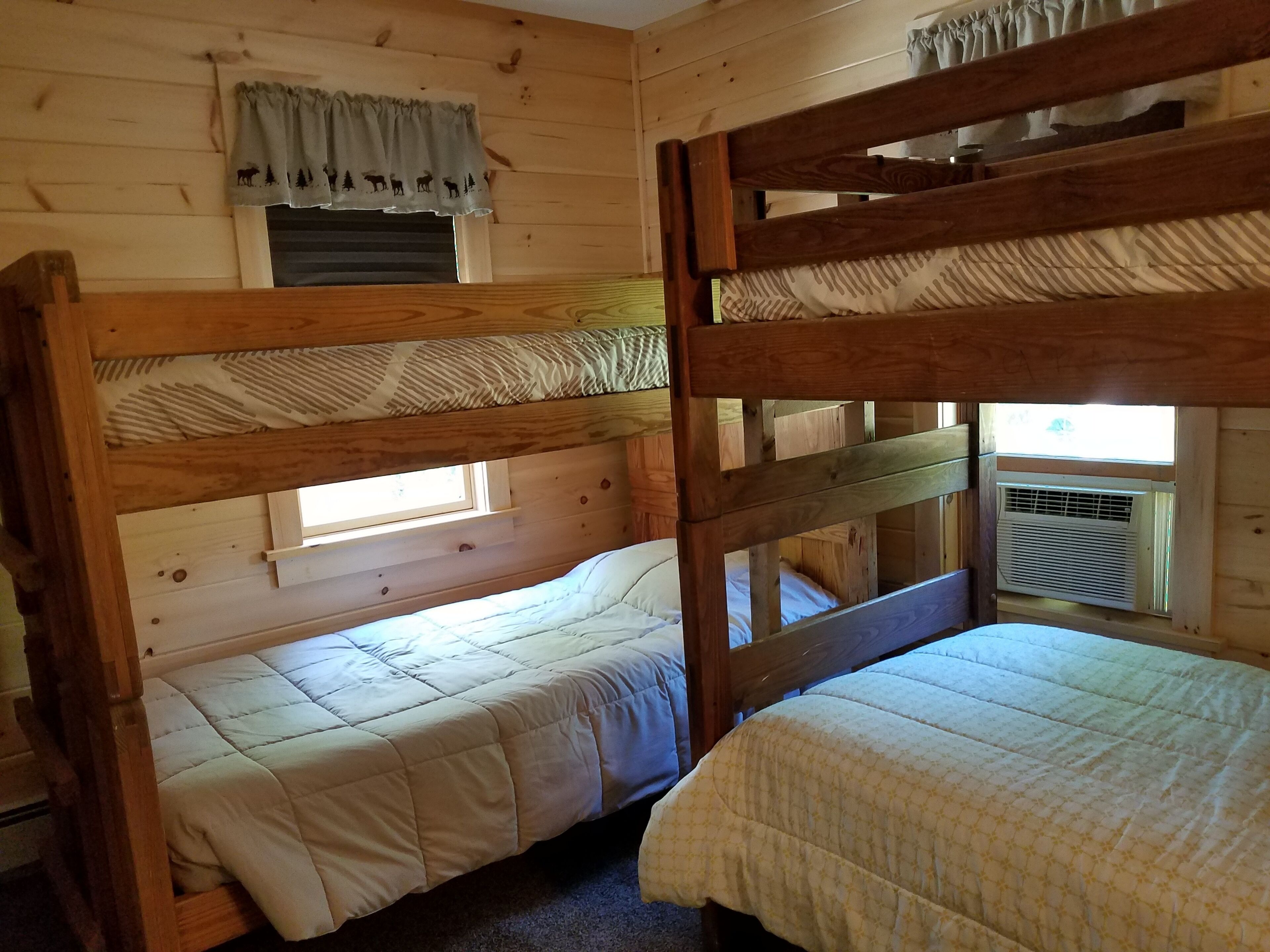 Una cabina con due letti a castello, una finestra con tenda e un condizionatore d'aria.