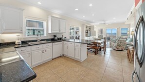 A spacious kitchen with white cabinetry, a black countertop, and a dining area with a table and chairs. - Sundancer, East. Beachfront 5BR Pool! PERFECT location. 😎 (Gulf Shores)