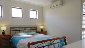 Ein Schlafzimmer mit einem Bett, zwei Nachttischen mit Lampen, einem Fenster mit Jalousien und einer Klimaanlage.