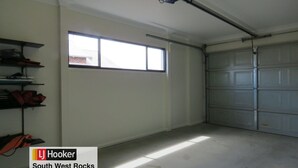 Eine Garage mit großem Fenster, geschlossenem Garagentor und Regalen mit Gegenständen an der linken Wand.