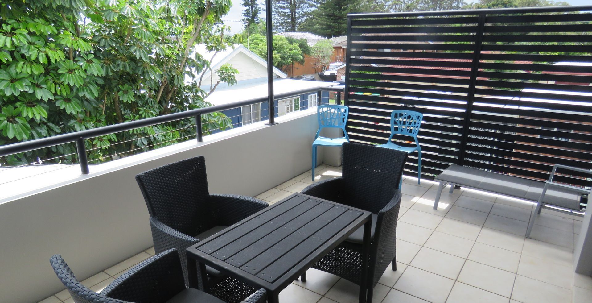 Uma varanda com mesa e cadeiras, uma cadeira azul e uma grade de metal.
