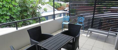 Uma varanda com mesa e cadeiras, uma cadeira azul e uma grade de metal.