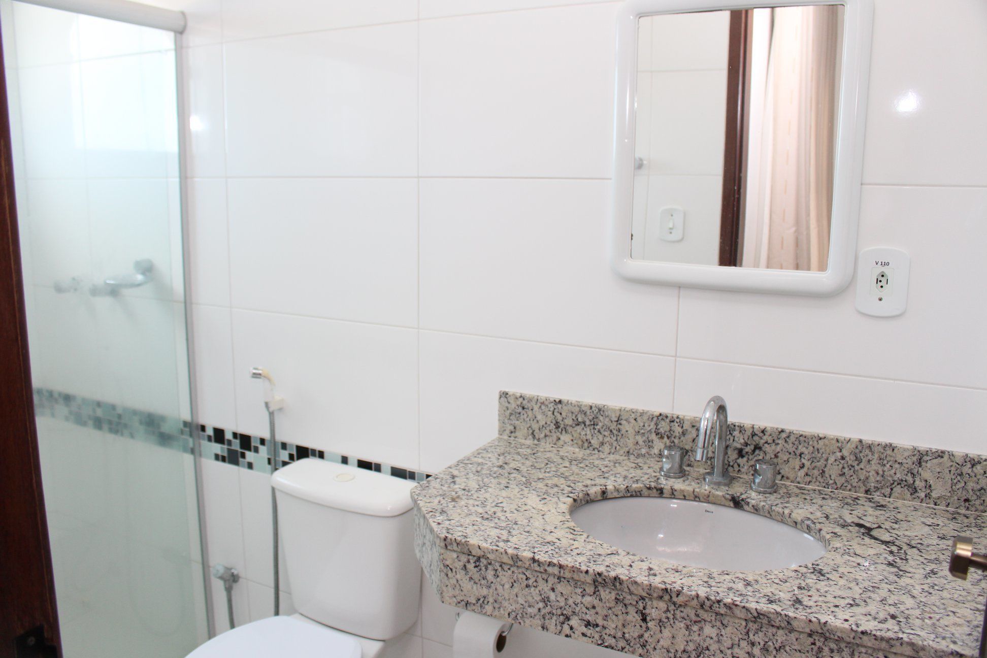 A bathroom with a white toilet, a granite sink, a mirror, and a shower.