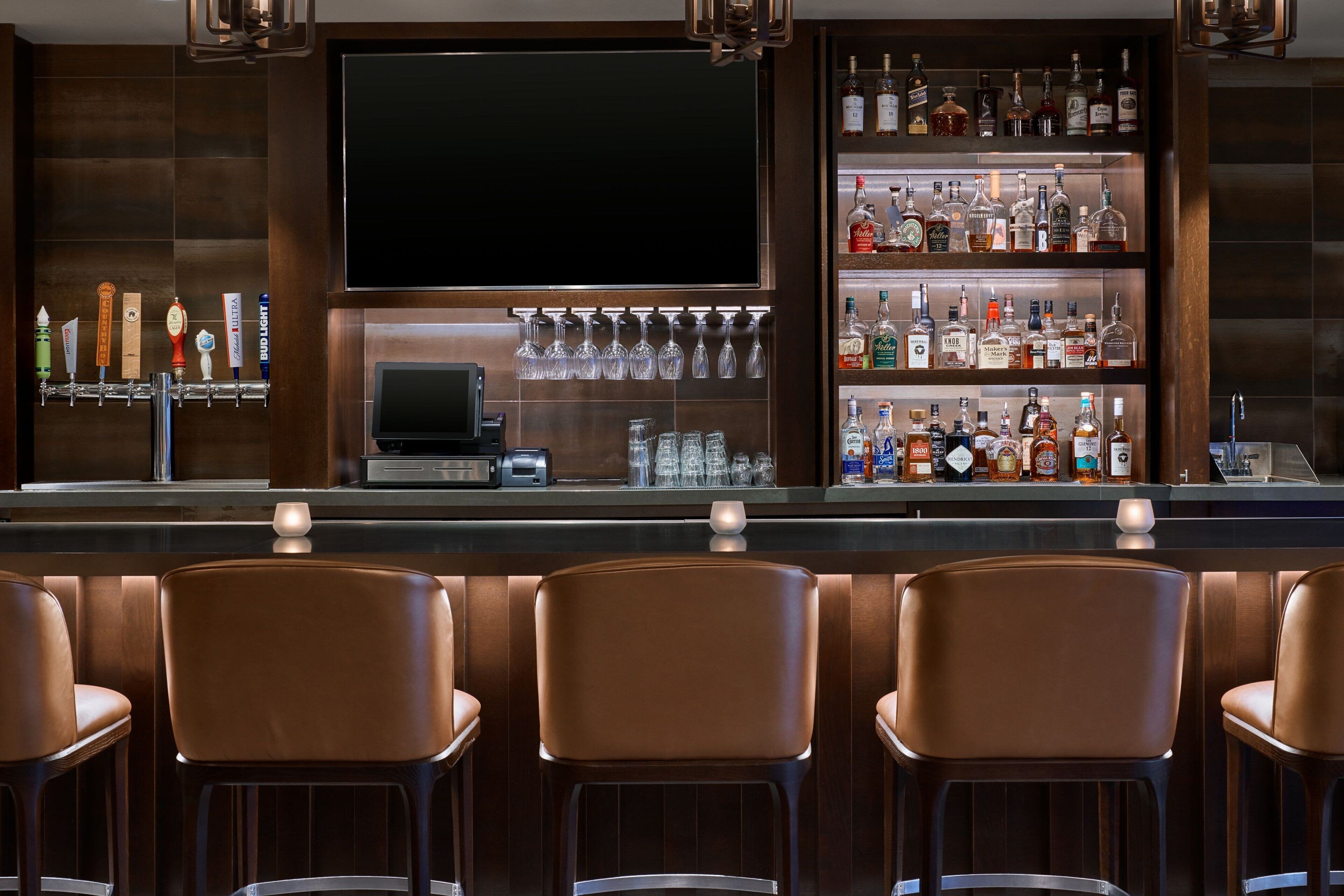 A bar area with a TV screen, a liquor display, and bar stools.