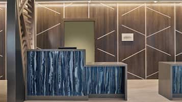 Un mostrador de recepción con diseño de mármol azul, una pared de paneles de madera con motivos geométricos, y un letrero que dice "RECEPTION".