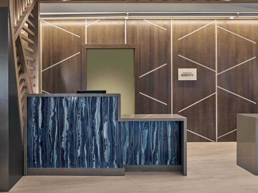 Un mostrador de recepción con diseño de mármol azul, una pared de paneles de madera con motivos geométricos, y un letrero que dice "RECEPTION".