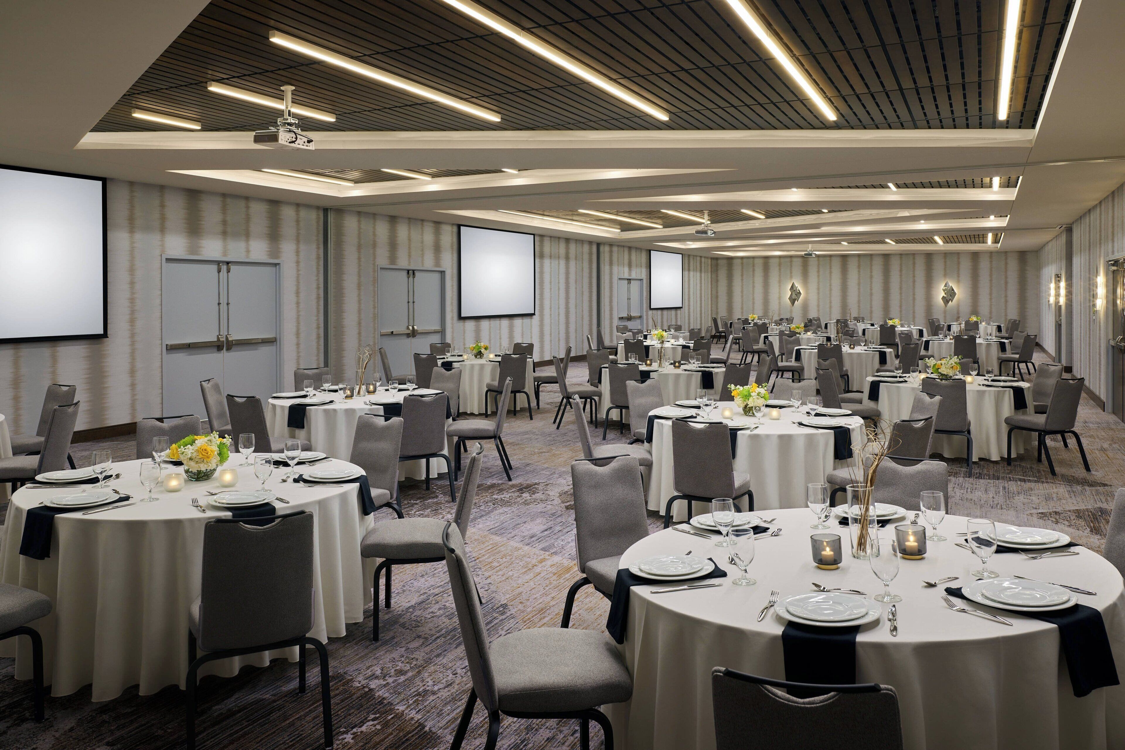 A conference room with multiple round tables, each set with white tablecloths, chairs, and floral centerpieces.