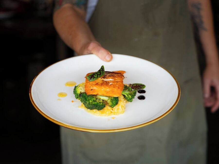 Een persoon houdt een bord eten vast, met onder meer broccoli en een stuk zalm.