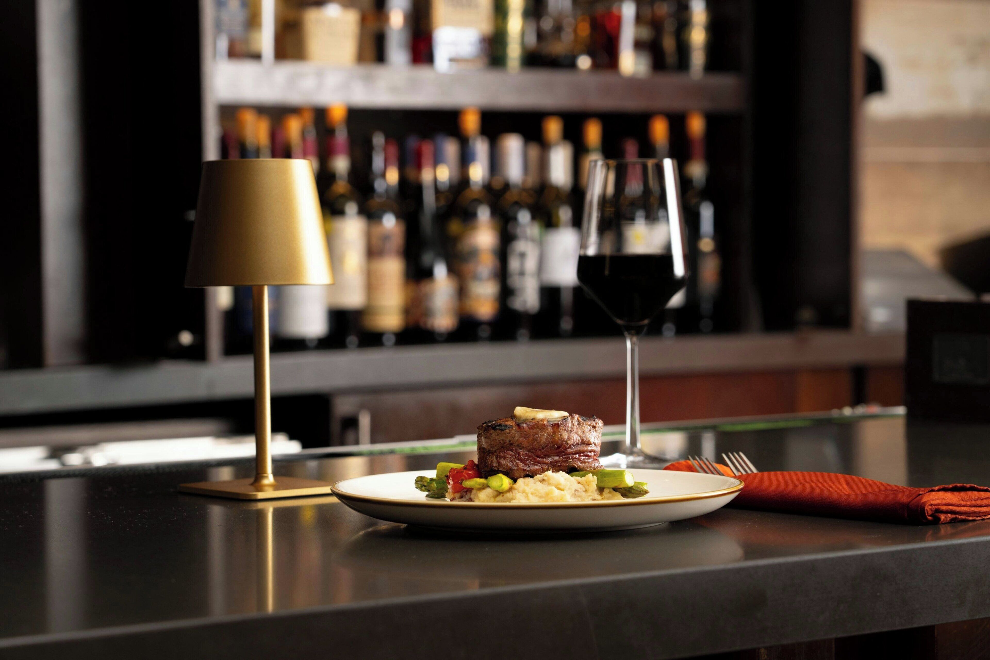 A well-lit dining area with a table set for a meal, a wine glass, and a lamp.