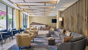 Un moderno vestíbulo de hotel con un amplio espacio de descanso, una recepción y grandes ventanales que ofrecen vistas al exterior.