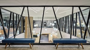 Un espacio de oficina moderno con una zona de estar central, separadores de vidrio y lámparas colgantes esféricas.