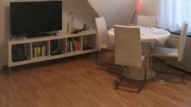 A modern living room with a flat-screen TV, a dining table with chairs, and a bookshelf. - Vacation apartment Harmonie 45 m2 (Solingen)