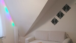 A living room with a sofa, a small wooden table, a lamp, and a wall with geometric patterns. - Vacation apartment Harmonie 45 m2 (Solingen)