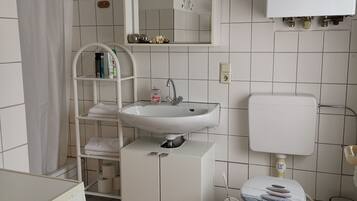 A bathroom with a white sink, mirror, toilet, and a pink rug.