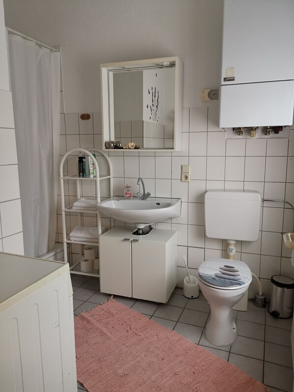 Une salle de bain avec un lavabo blanc, un miroir, des toilettes et un tapis rose.