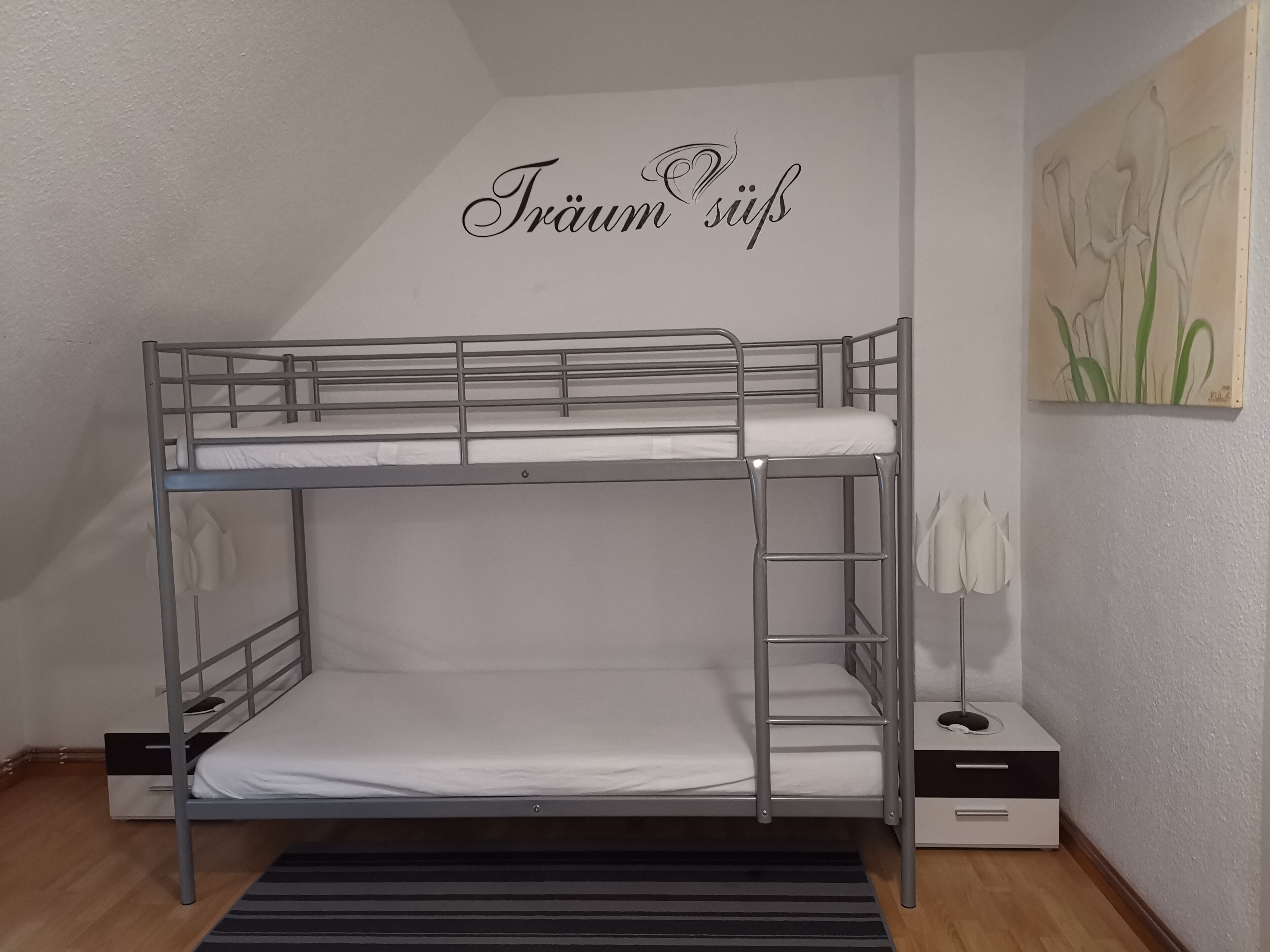 A bunk bed with a ladder, a small bedside table, and a wall-mounted artwork.