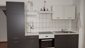 A modern kitchen with a built-in oven, a sink, and a refrigerator. There are cabinets, a countertop, and a shelf with decorative items. - Vacation apartment Harmonie 45 m2 (Solingen)