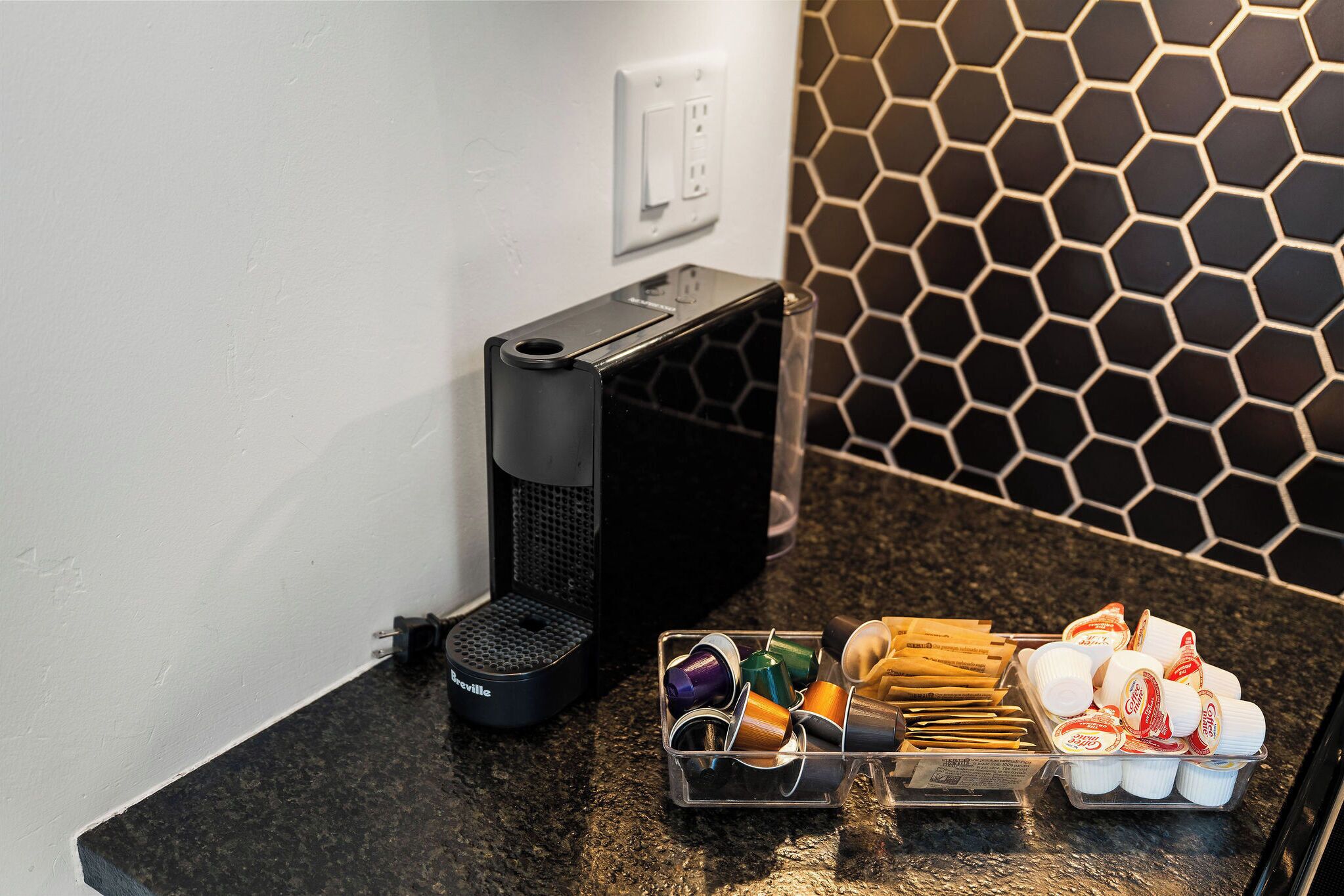 Un comptoir de cuisine avec une machine à café, un récipient contenant des capsules de café et un plateau avec des aliments emballés.