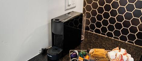 Un comptoir de cuisine avec une machine à café, un récipient contenant des capsules de café et un plateau avec des aliments emballés.