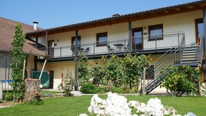 A two-story building with a balcony, a staircase, and a garden with flowers and plants. - Vacation apartment Blumenwiese - Preuschens Hof (Egloffstein)