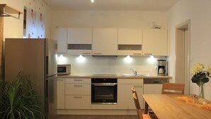 A modern kitchen with white cabinets, stainless steel appliances, and a wooden dining table. - Vacation apartment Blumenwiese - Preuschens Hof (Egloffstein)