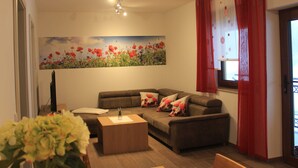 A living room with a sofa, a coffee table, and a painting of red flowers on the wall. - Vacation apartment Blumenwiese - Preuschens Hof (Egloffstein)