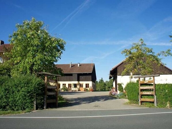 A rural property with a paved driveway leading to a building with a dark roof and white walls.