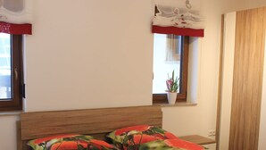 A bedroom with a wooden headboard, a window with a plant, and a red curtain. - Vacation apartment Blumenwiese - Preuschens Hof (Egloffstein)