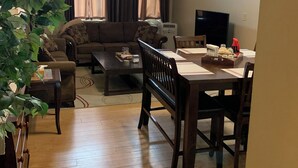 Un salon comprenant un canapé, une table basse, une table à manger avec des chaises, un ventilateur de plafond et une grande plante.