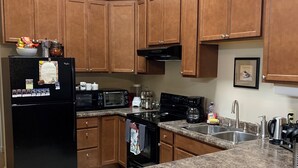 Une cuisine avec des meubles de rangement en bois, un réfrigérateur noir, un four à micro-ondes, une cuisinière et un évier.