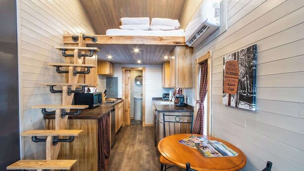 Cocina compacta con armarios de madera, una mesa de comedor y una cama de altillo.