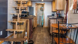 Cocina compacta con armarios de madera, comedor con sillas metálicas y un dormitorio en entrepiso con cama y almohadas.