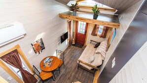 Habitación pequeña con sofá, una mesa redonda y televisor. Cuenta con una ventana con cortinas y una puerta.