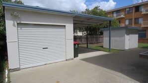 En garage med en lukket, hvid dør, et overdækket parkeringsområde og et lille udhus.