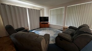 A living room with a flat-screen TV, two recliner sofas, a patterned rug, and a wooden cabinet.