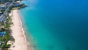 Vista aèria d'una platja amb aigües turqueses cristal·lines, una riba sorrenca i una zona de turisme amb edificis i palmeres.