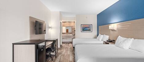 A hotel room with two beds, a desk, a TV, and a bathroom visible through an open door.