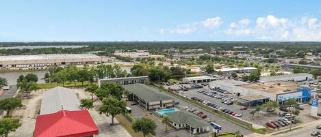 An aerial view of a commercial area with a parking lot, a red-roofed building, and a large warehouse.