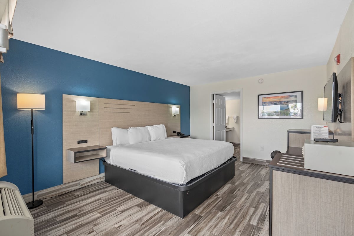 A hotel room with a bed, bedside table, lamp, and a desk with a chair.
